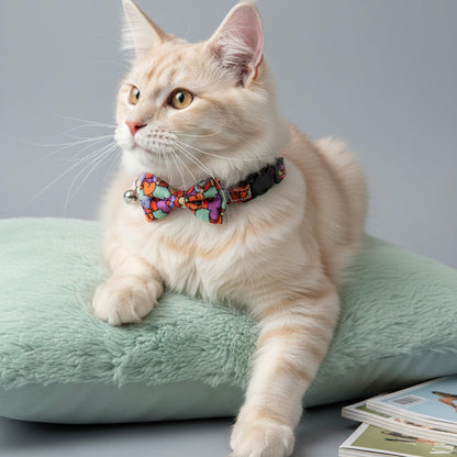 Cream cat wearing Bling Fuzzie Colorful Hearts Cat Collar with multicolor bow tie and silver bell, resting on a mint green plush cushion beside a magazine, lifestyle product photo
