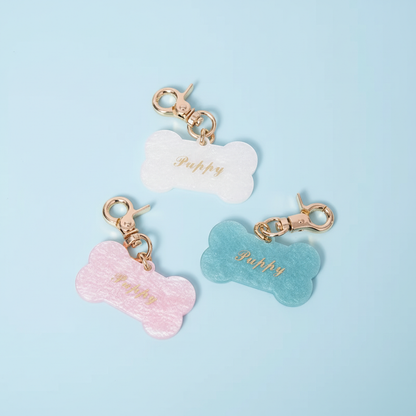 Custom dog bone pet ID tags collection in pink, white, and blue glitter acetate with gold foil lettering on light blue background