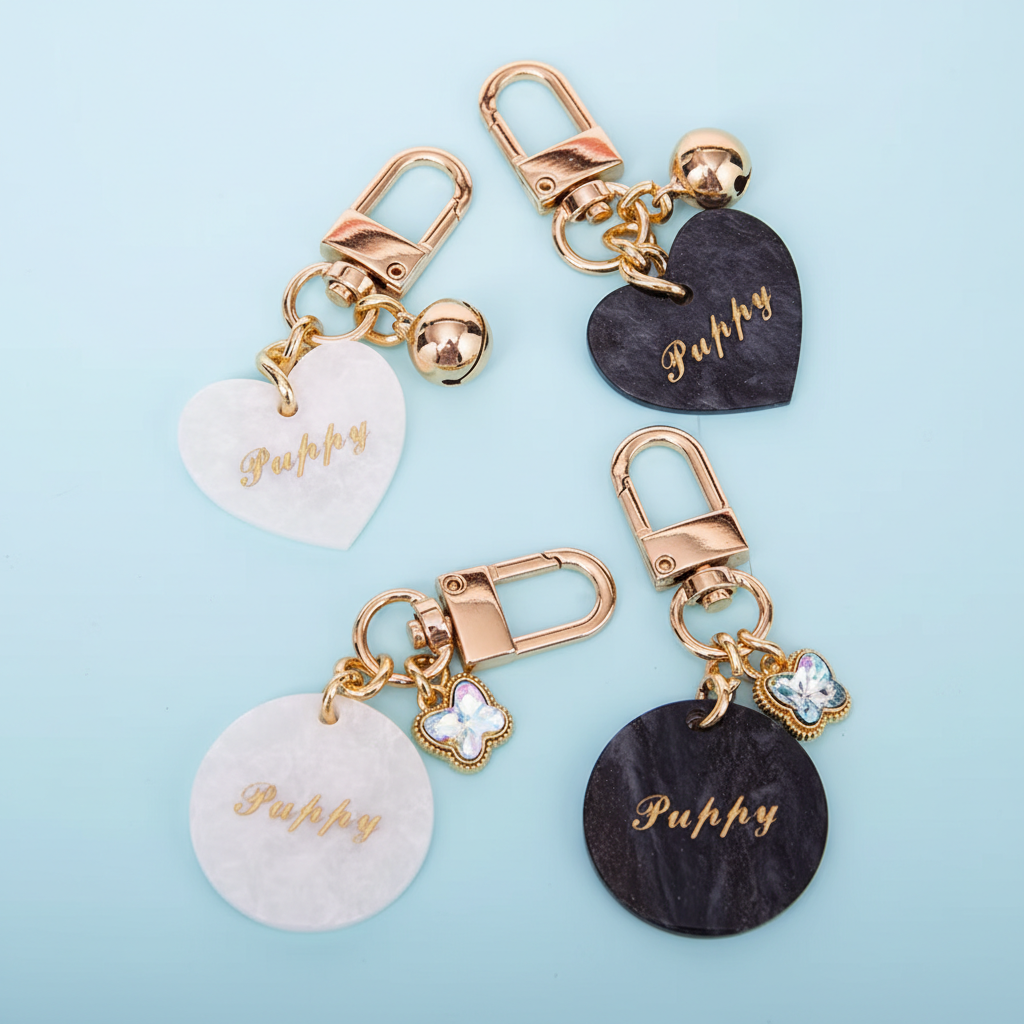 Custom acetate pet ID tags collection showing heart and round shapes with gold foil lettering, crystal clover and gold bell charms on light blue background
